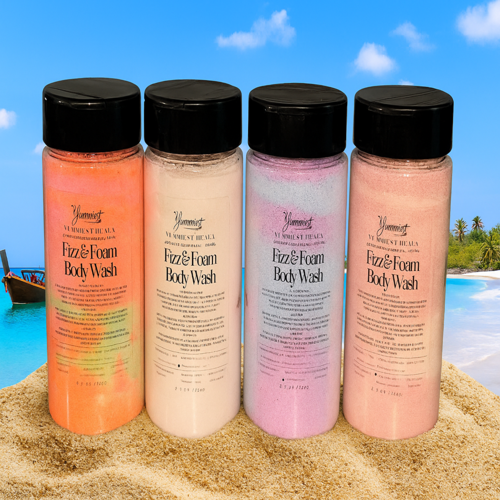 Four bottles of Yummie Fizz & Foam Body Wash on a sandy beach with a blue sky and ocean in the background.